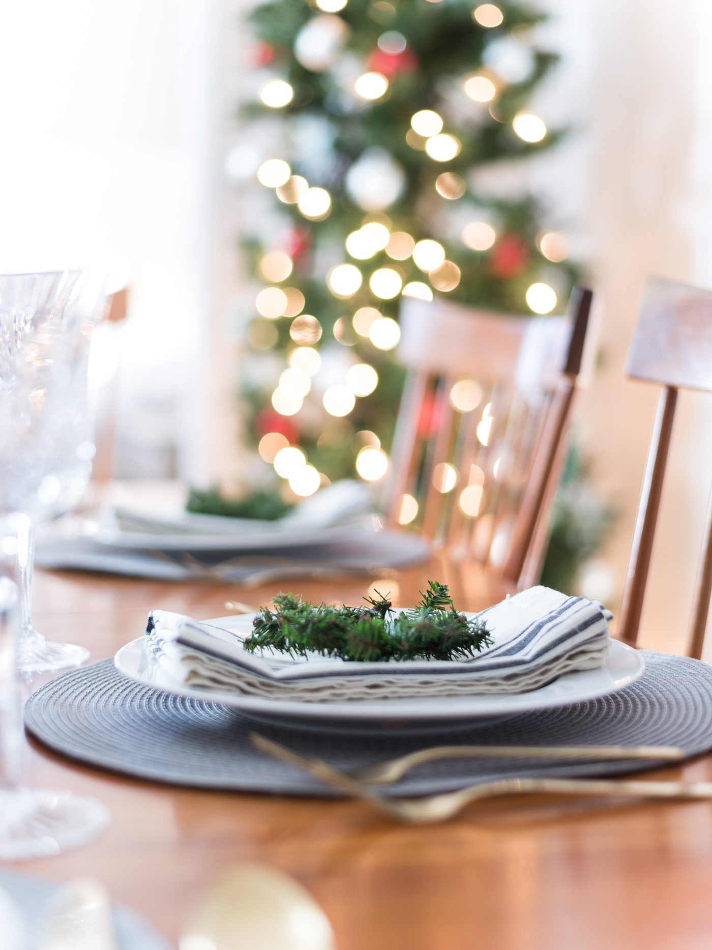 Christmas Table Setting in Gray, White, Gold. Gray and White Holiday Table Setting Idea. Mini Wreath Holiday Place Setting Idea. White mini Christmas Trees and Tapered Candles Holiday Table Centerpiece.