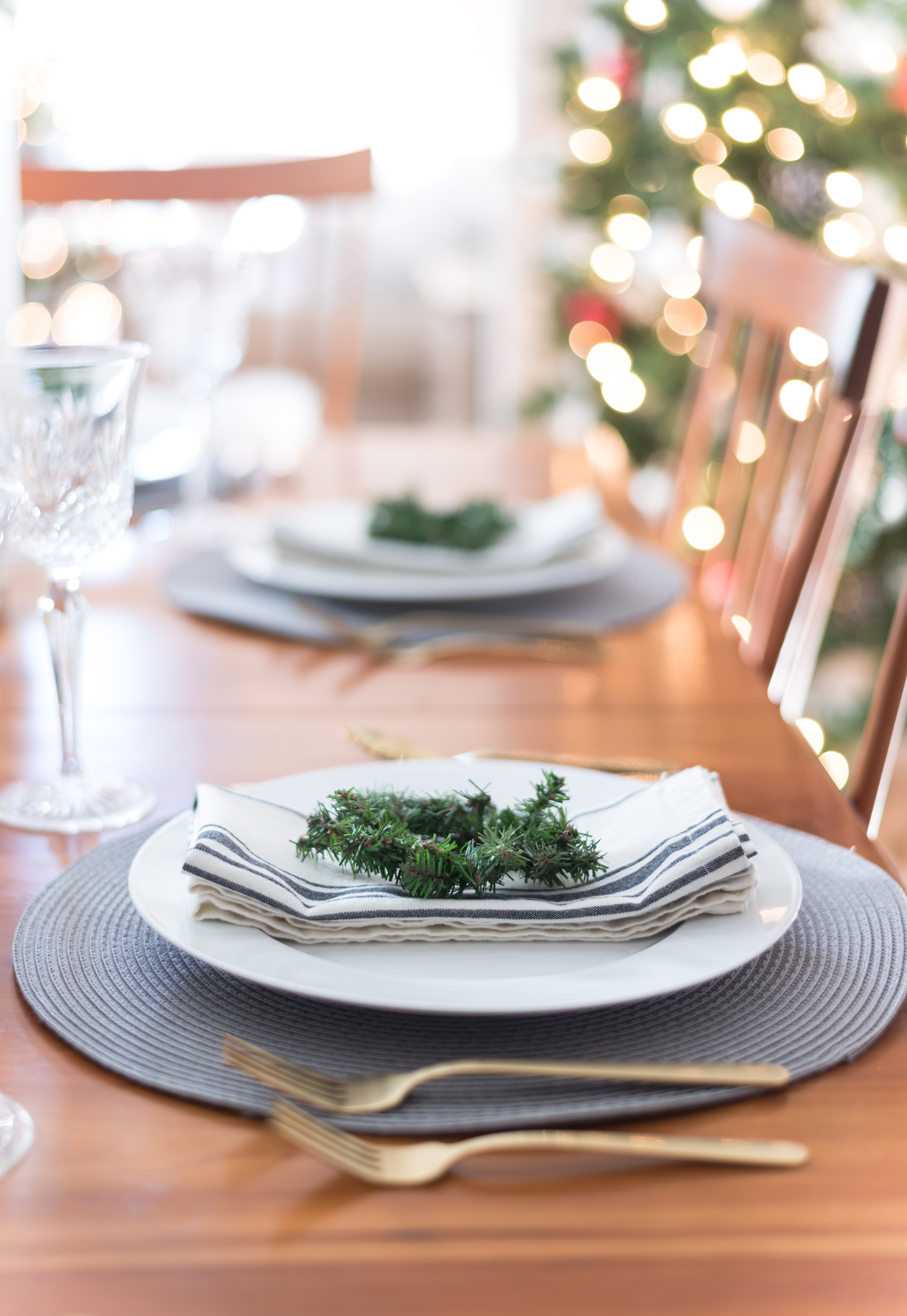 Christmas Table Setting in Gray, White, Gold. Gray and White Holiday Table Setting Idea. Mini Wreath Holiday Place Setting Idea. White mini Christmas Trees and Tapered Candles Holiday Table Centerpiece.