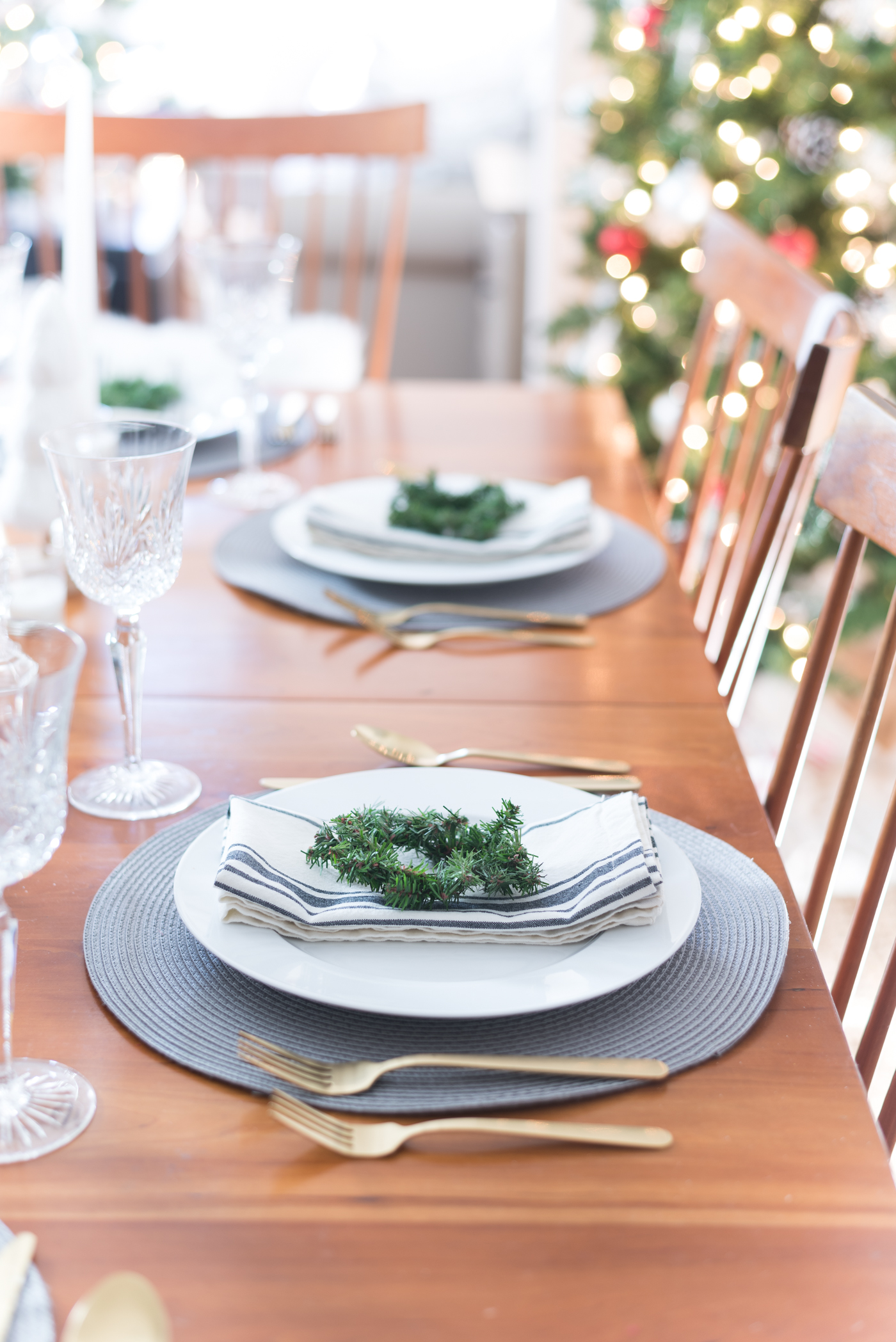 Christmas Table Setting in Gray, White, Gold. Gray and White Holiday Table Setting Idea. Mini Wreath Holiday Place Setting Idea. White mini Christmas Trees and Tapered Candles Holiday Table Centerpiece.