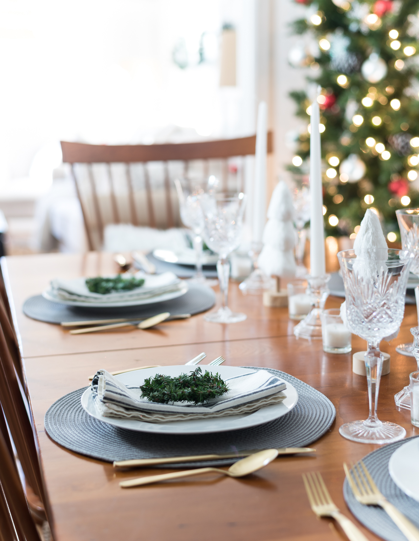 Christmas Table Setting in Gray, White, Gold. Gray and White Holiday Table Setting Idea. Mini Wreath Holiday Place Setting Idea. White mini Christmas Trees and Tapered Candles Holiday Table Centerpiece.