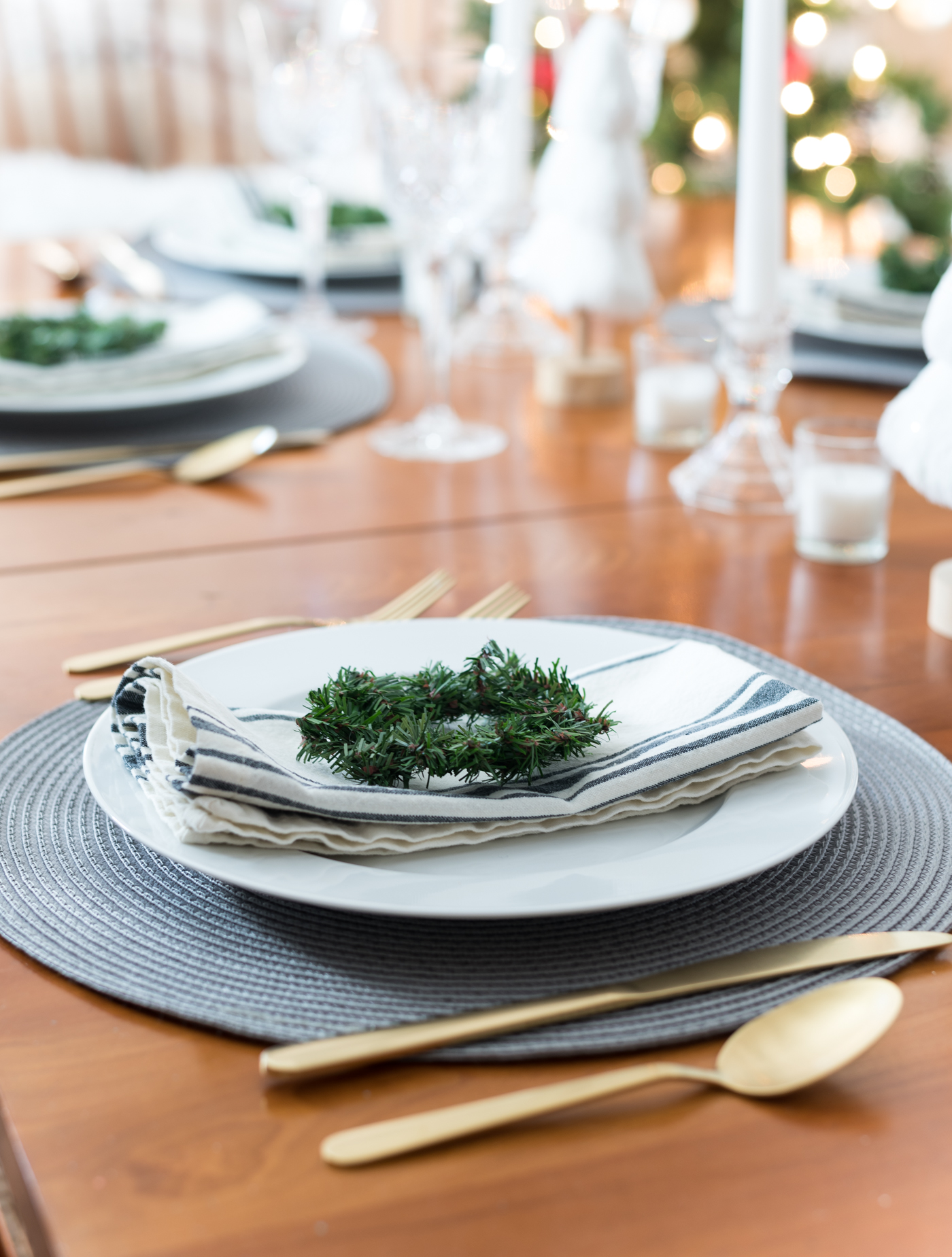 Christmas Table Setting in Gray, White, Gold. Gray and White Holiday Table Setting Idea. Mini Wreath Holiday Place Setting Idea. White mini Christmas Trees and Tapered Candles Holiday Table Centerpiece.