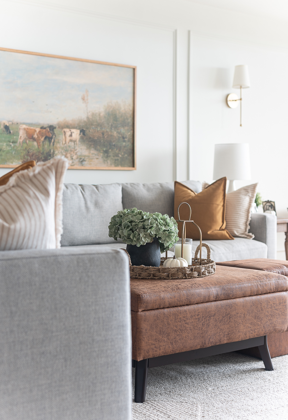 Fall Living Room in Rust, Brown, Mustard, Black, Gray, Neutral. Mustard PIllow. Faux Leather Ottomon from Amazon. Crate & Barrel Barrett Sectional Sofa. Pottery Barn TV Console. Wayfair Side Tables in Light Wood. Vintage Cow Print on Canvas.